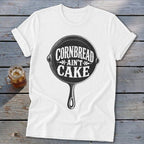 White t-shirt with black graphic of cast iron skillet reading "Cornbread Ain't Cake".
