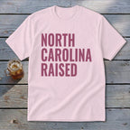 Pink t-shirt with "NORTH CAROLINA RAISED" text in burgundy.
