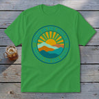 A green t-shirt featuring a circular graphic with mountains, a rising sun, and text that reads BORN IN THE HOLLER RAISED ON THE RIDGE.