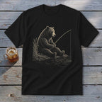 Black t-shirt featuring a bear fishing by a lake with reeds and a drink.