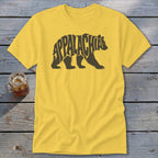 A yellow t-shirt with a black bear graphic formed by the word Appalachia on a wooden background.