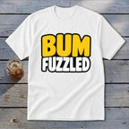 A white t-shirt featuring the text BUM FUZZLED on a wooden surface.
