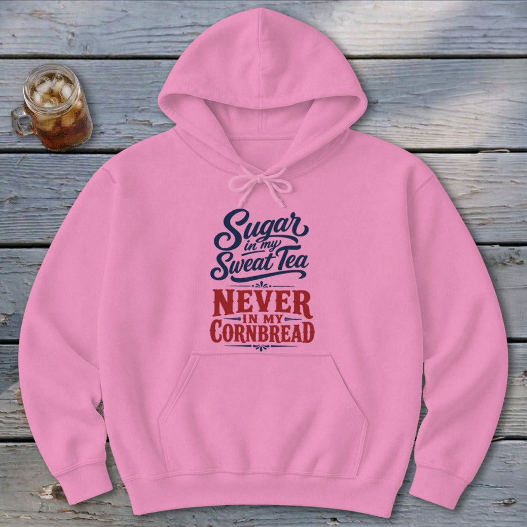 Pink hooded sweatshirt with front pocket and text reading Sugar in my Sweet Tea NEVER IN MY CORNBREAD on a wooden background.