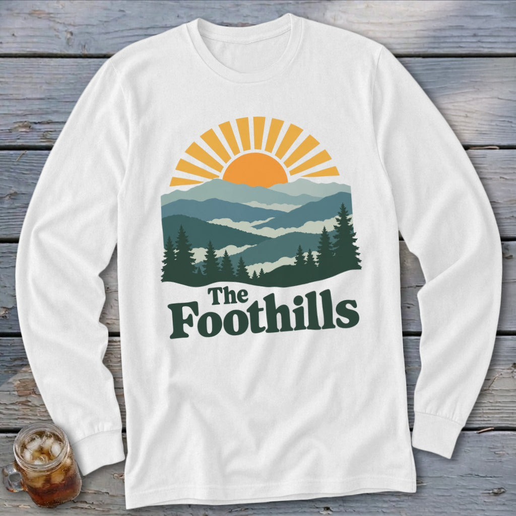 White long-sleeve shirt with "The Foothills" text and a mountain sunset graphic.