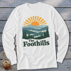 White long-sleeve shirt with "The Foothills" text and a mountain sunset graphic.