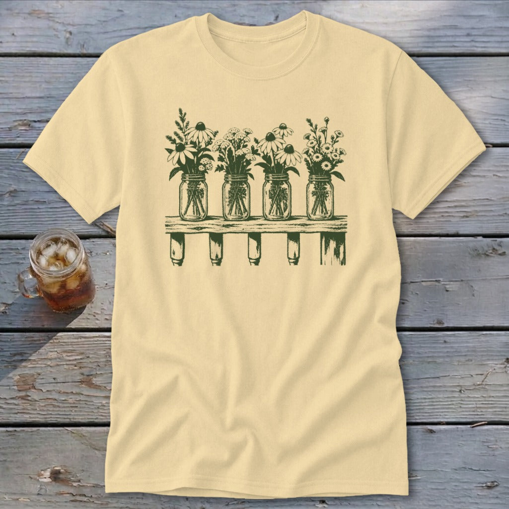 Light yellow short-sleeved t-shirt with a green graphic of four mason jars filled with wildflowers on a shelf.