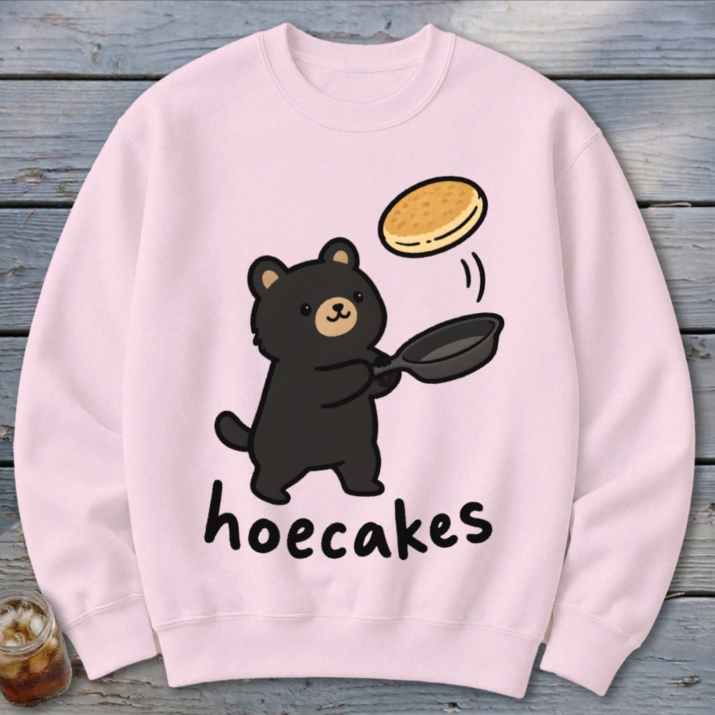 Light pink crewneck sweatshirt featuring a cartoon black bear flipping a pancake and the text hoecakes.