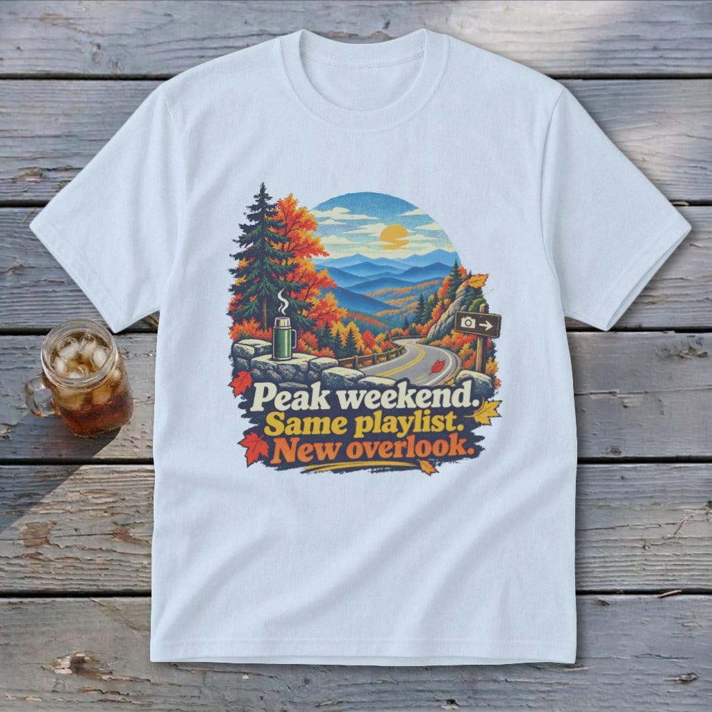T-shirt graphic with mountains, road, and text "Peak weekend. Same playlist. New overlook."