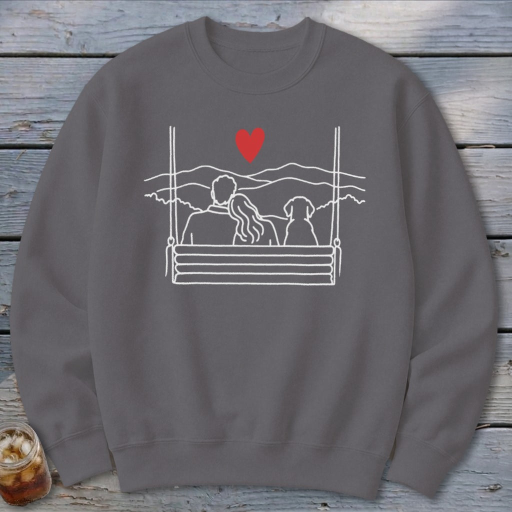 Gray sweatshirt with line art of couple and dog on swing with mountains and heart.