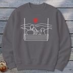Gray sweatshirt with line art of couple and dog on swing with mountains and heart.
