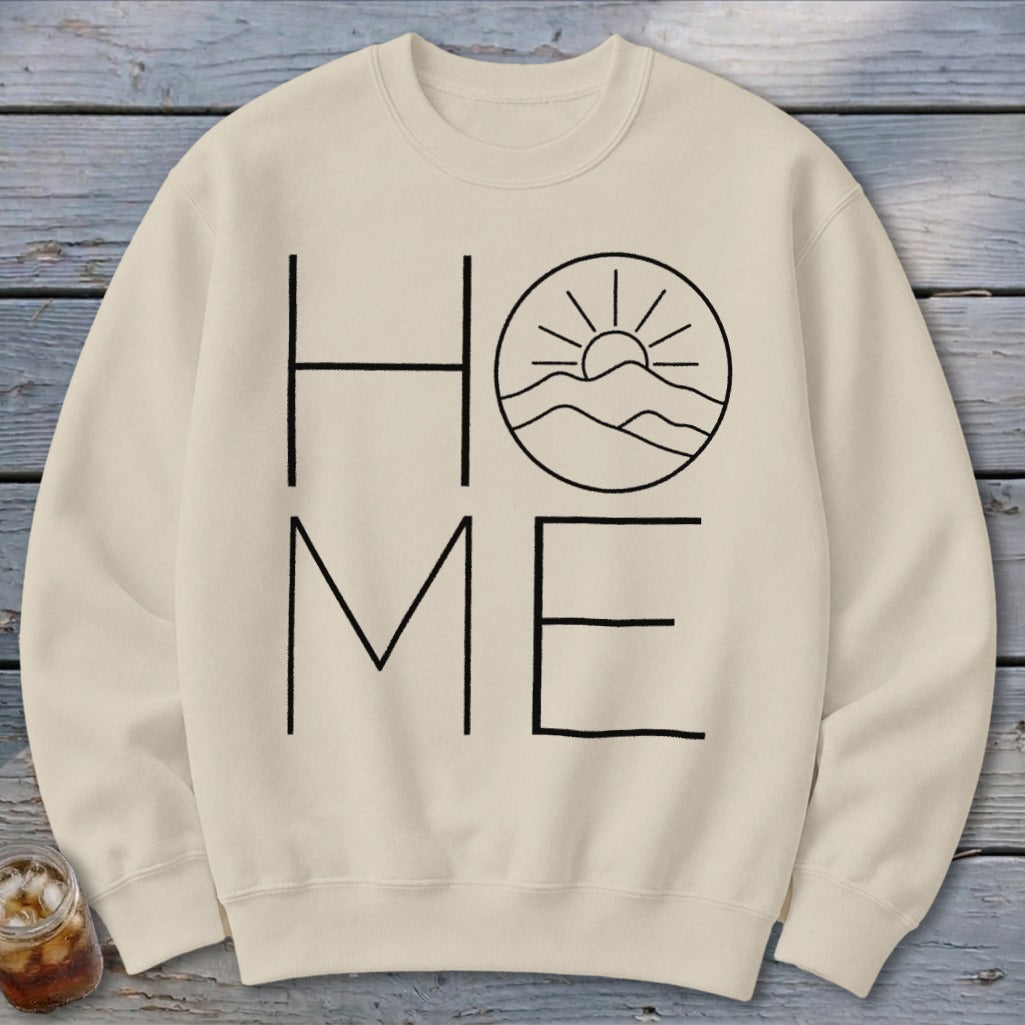Beige crewneck sweatshirt featuring a black graphic that spells HOME, with a mountain and sun scene replacing the letter O.