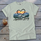 Light green t-shirt with a heart framing a mountain sunrise and "Appalachia Strong" text.