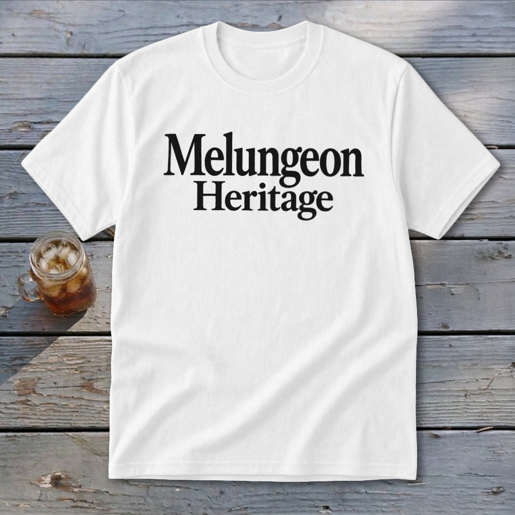 White t-shirt with black text reading Melungeon Heritage centered on the chest, lying on a wooden surface.
