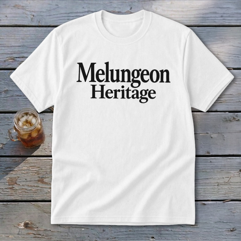 White t-shirt with black text reading Melungeon Heritage centered on the chest, lying on a wooden surface.