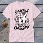 Pink t-shirt with black graphic of feet in water and text "Barefoot on the Crick Bank".