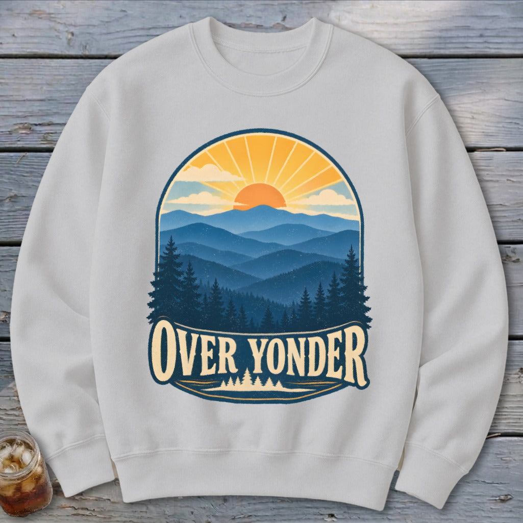 Light grey crewneck sweatshirt featuring a graphic of blue mountain ranges, pine trees, and a setting sun with the text Over Yonder.
