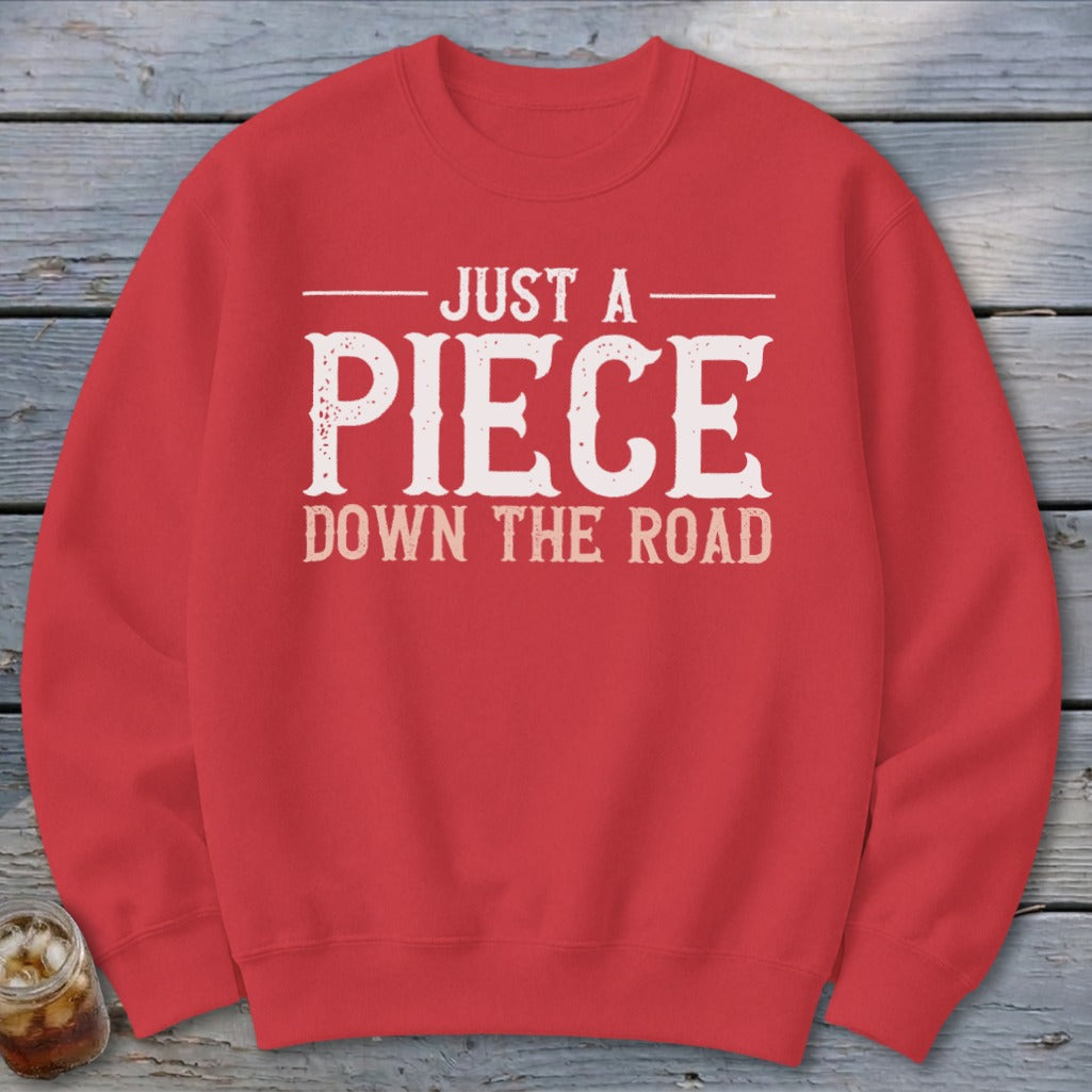 Red crewneck sweatshirt with white text reading "JUST A PIECE DOWN THE ROAD".