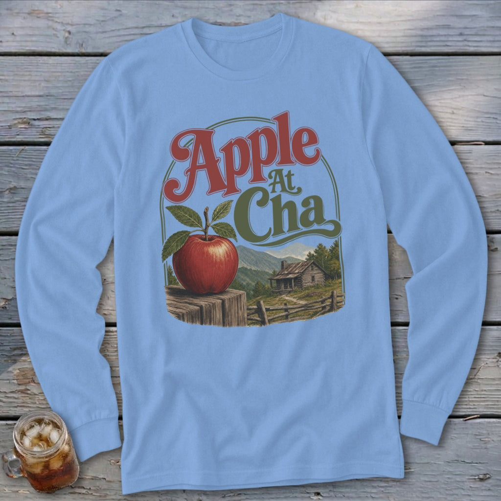 Light blue long-sleeve t-shirt with a vintage graphic featuring an apple, a cabin, and text.