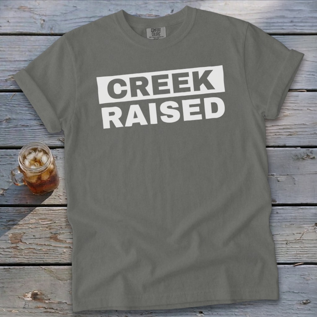 Gray t-shirt with white text that reads "CREEK RAISED" in a box.