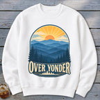 A white crewneck sweatshirt featuring a graphic of sunset mountains and the text Over Yonder.