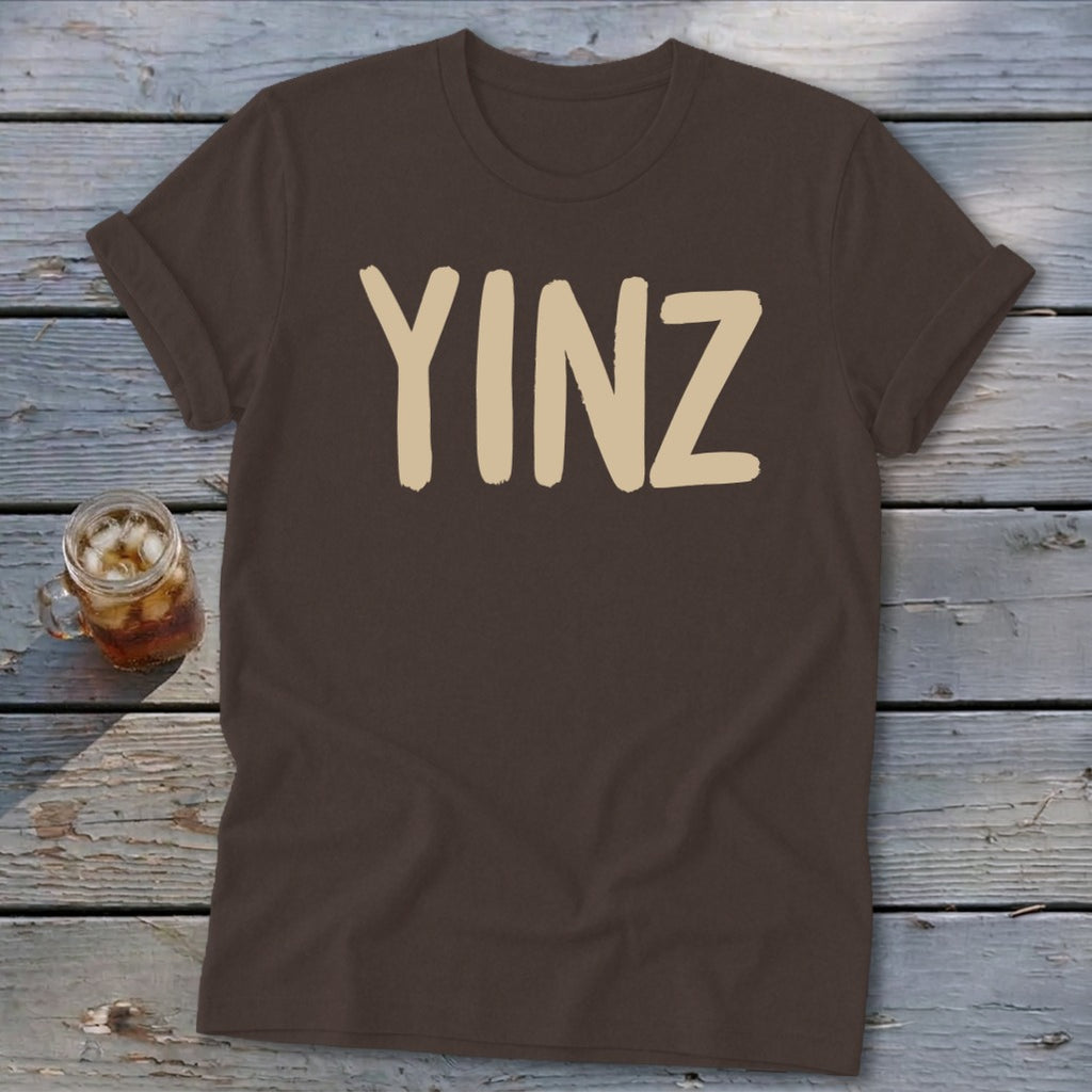 Brown t-shirt with beige "YINZ" text and a glass of iced drink.