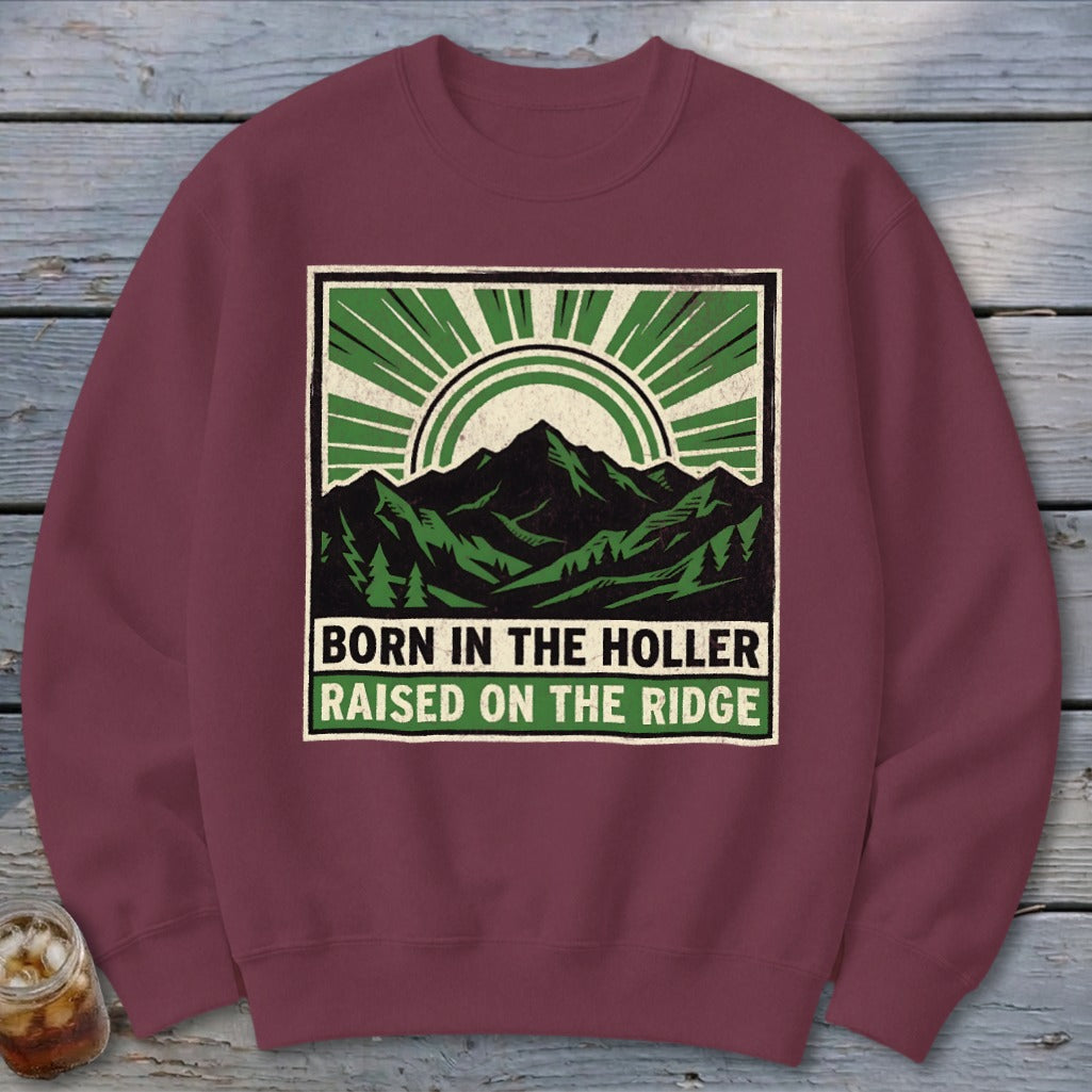 Maroon crewneck sweatshirt featuring a graphic of mountains and sunburst with text reading BORN IN THE HOLLER RAISED ON THE RIDGE.