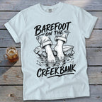 White t-shirt with "Barefoot on the Creek Bank" graphic of bare feet in water.
