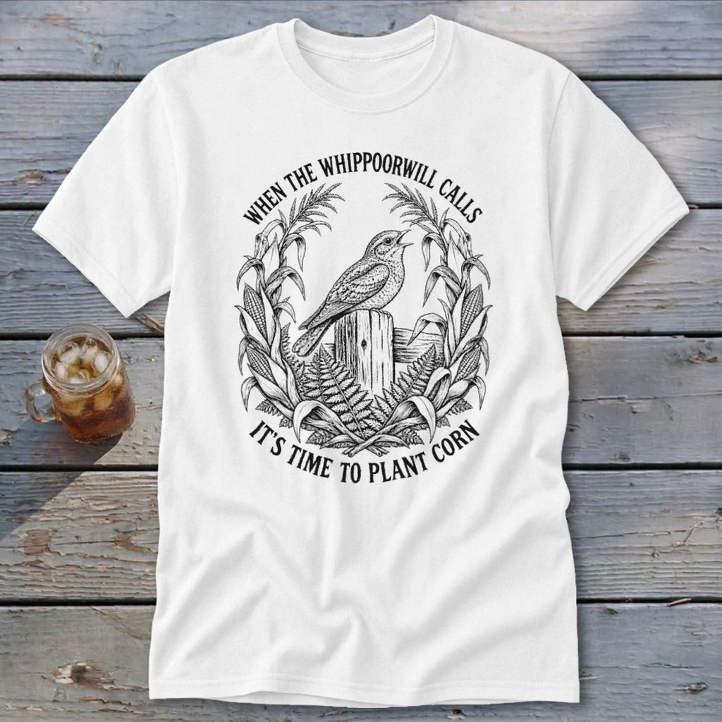 White t-shirt with a black vintage graphic of a bird, corn stalks, and text reading "WHEN THE WHIPPOORWILL CALLS IT'S TIME TO PLANT CORN".