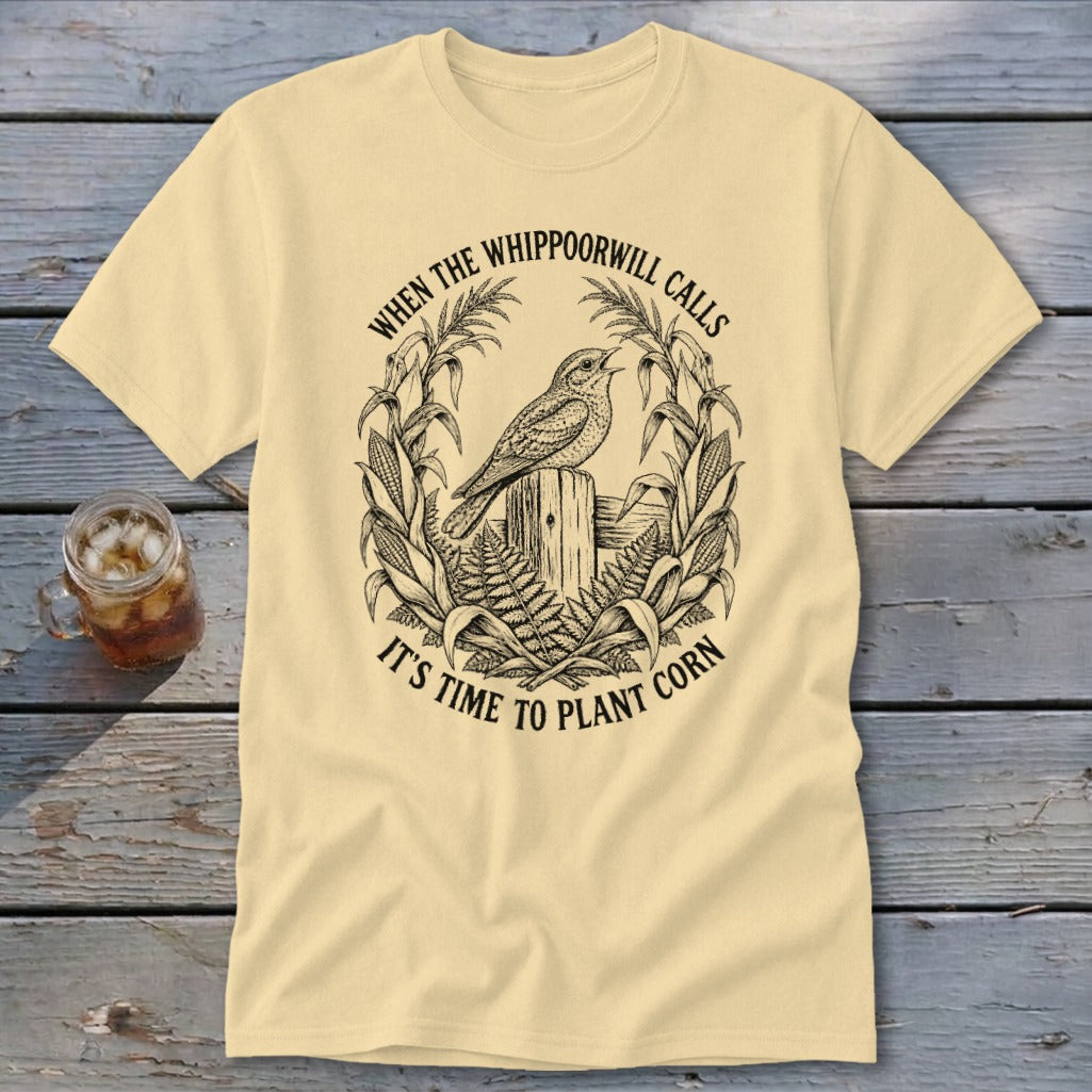 Cream-colored t-shirt with a black line art graphic of a bird on a fence post surrounded by corn.