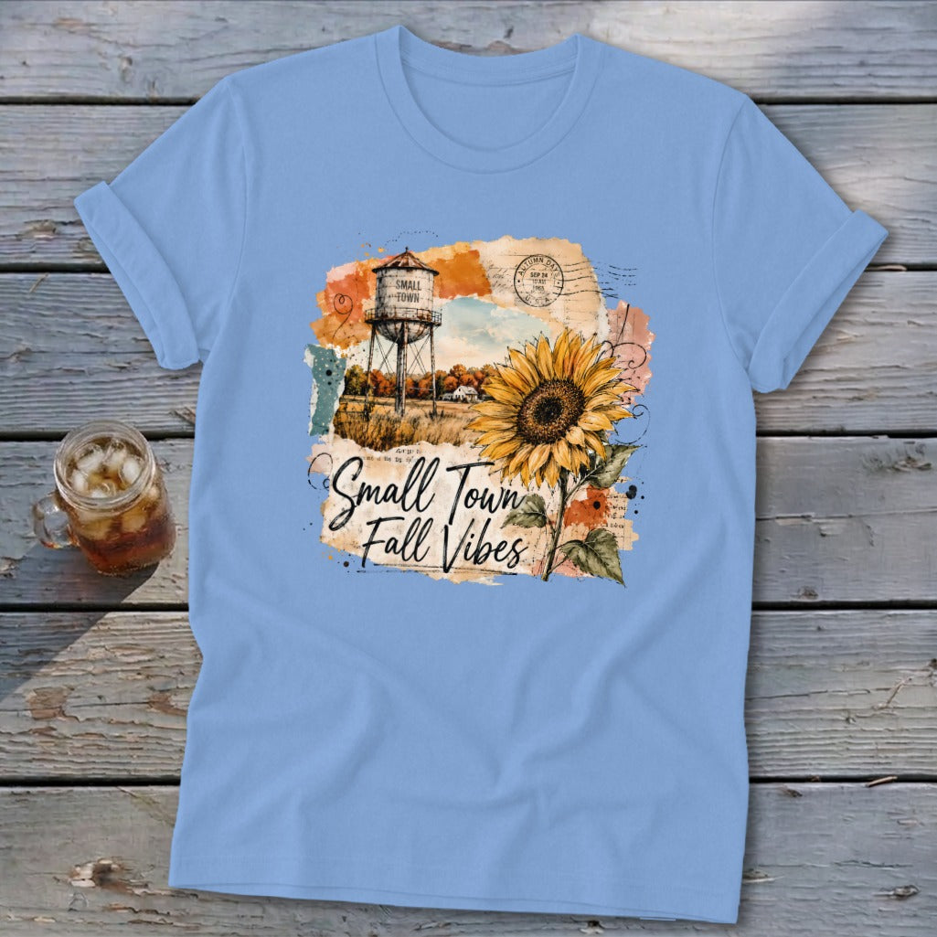 Light blue t-shirt with a watercolor graphic of a water tower, sunflower, and the text "Small Town Fall Vibes."