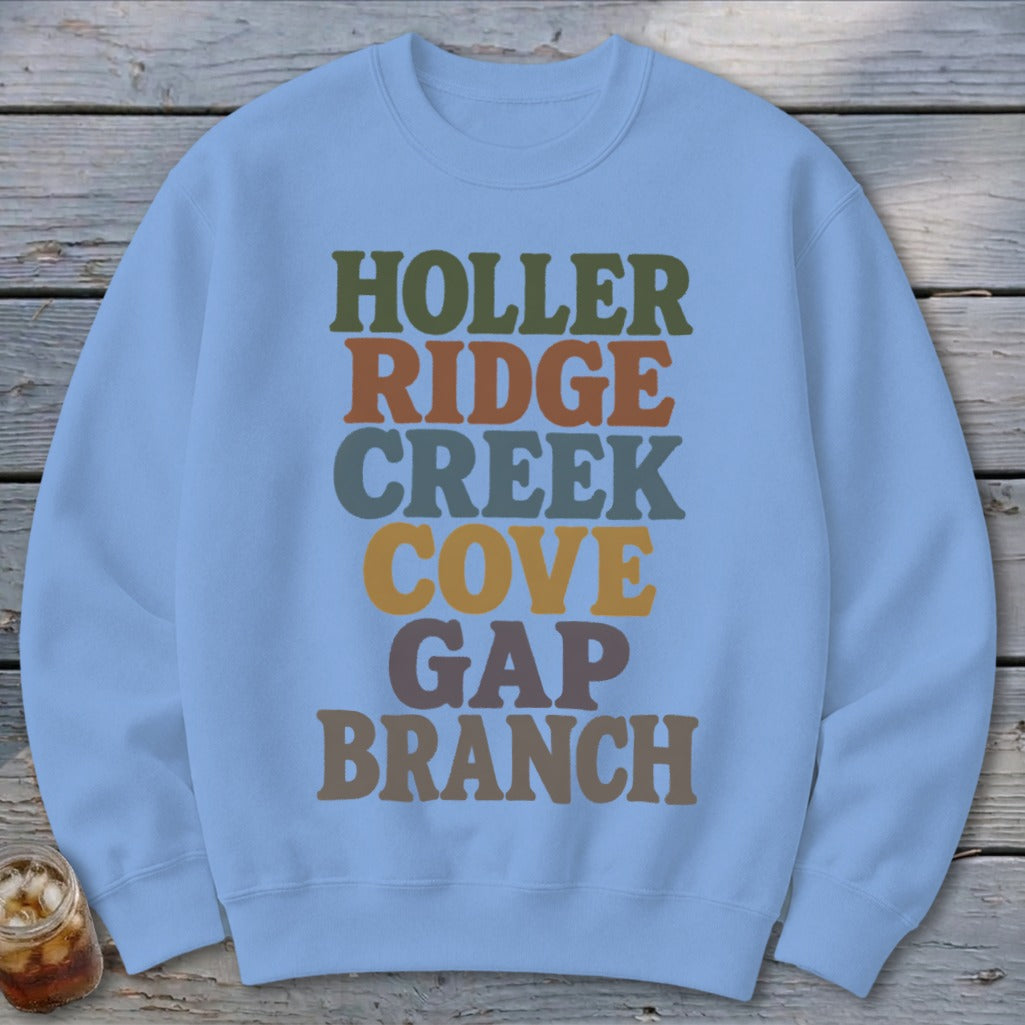 Light blue crewneck sweatshirt featuring stacked multi-colored text that reads HOLLER RIDGE CREEK COVE GAP BRANCH.