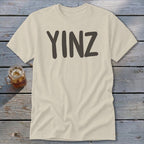 Cream t-shirt with "YINZ" printed in dark gray on the front.