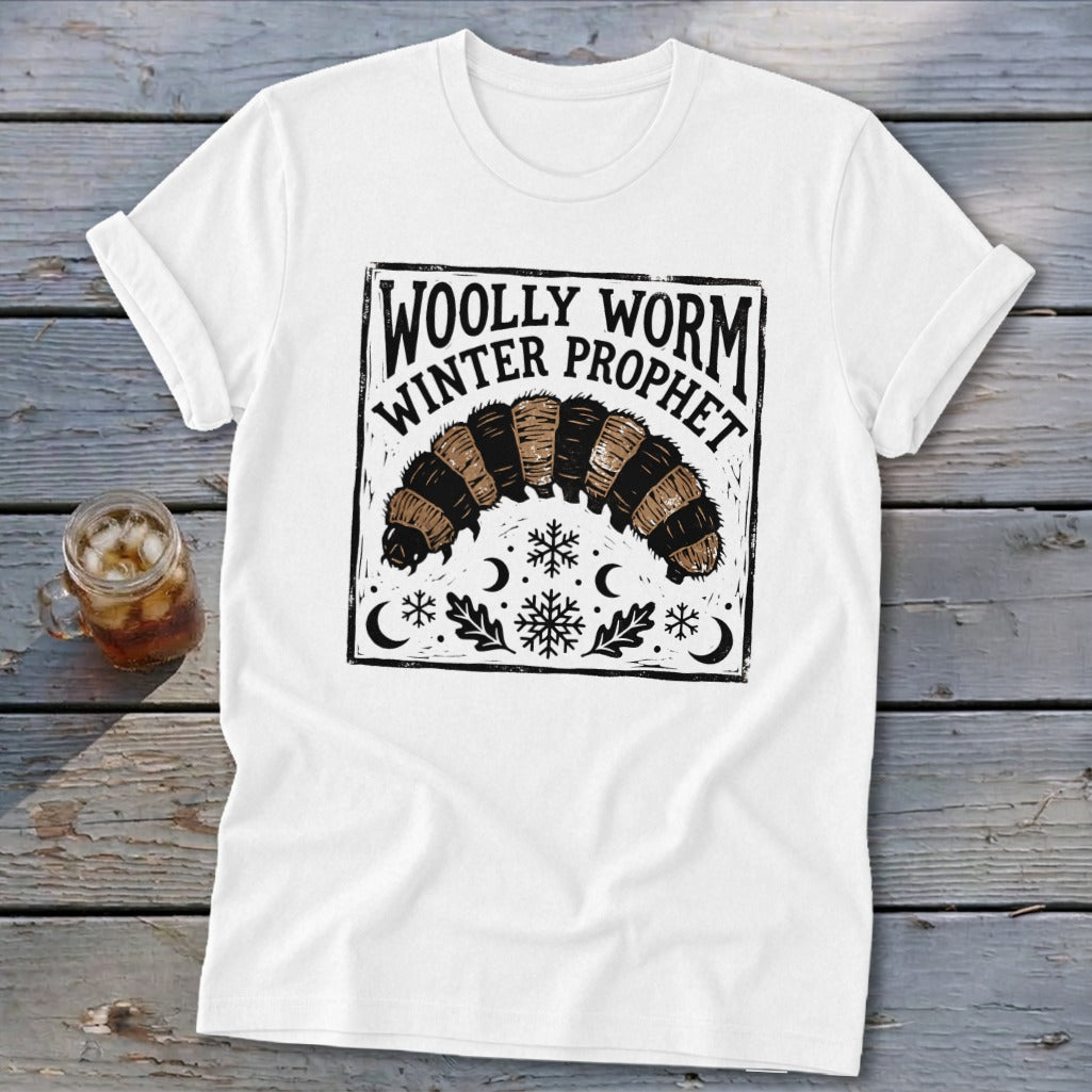 A white t-shirt featuring a black graphic of a woolly worm, snowflakes, moons, and text reading Woolly Worm Winter Prophet.