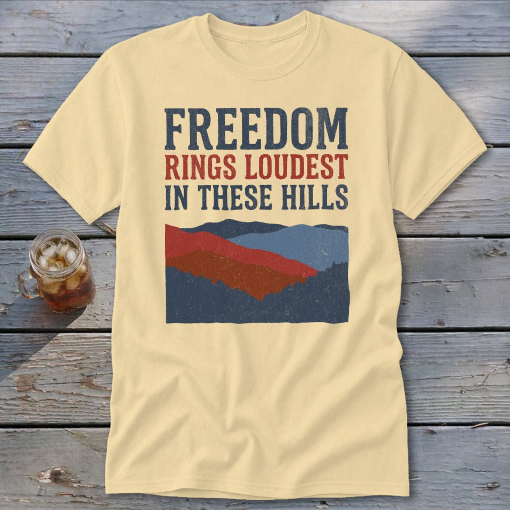 Cream t-shirt featuring distressed blue and red text reading Freedom Rings Loudest in These Hills above a mountain graphic.