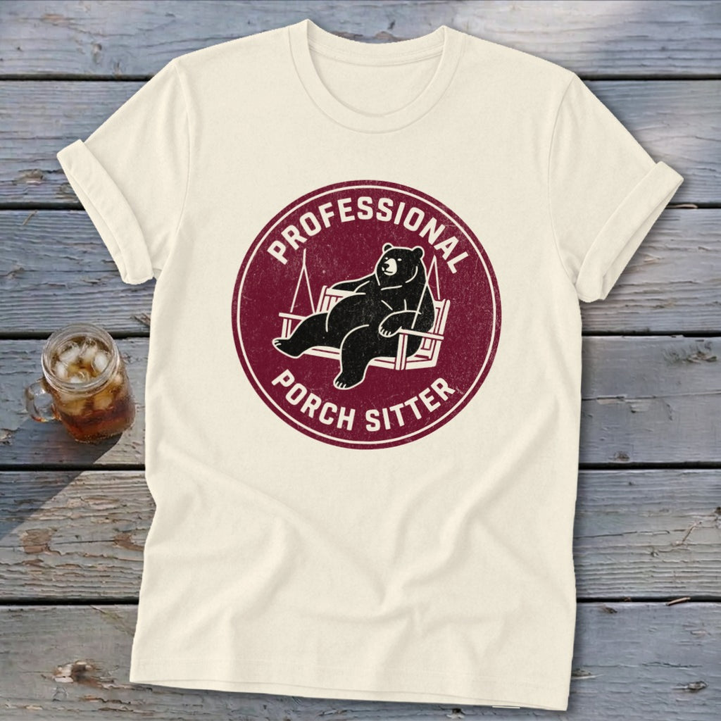 Cream t-shirt with a maroon circular graphic featuring a bear relaxing on a porch swing and the text Professional Porch Sitter.