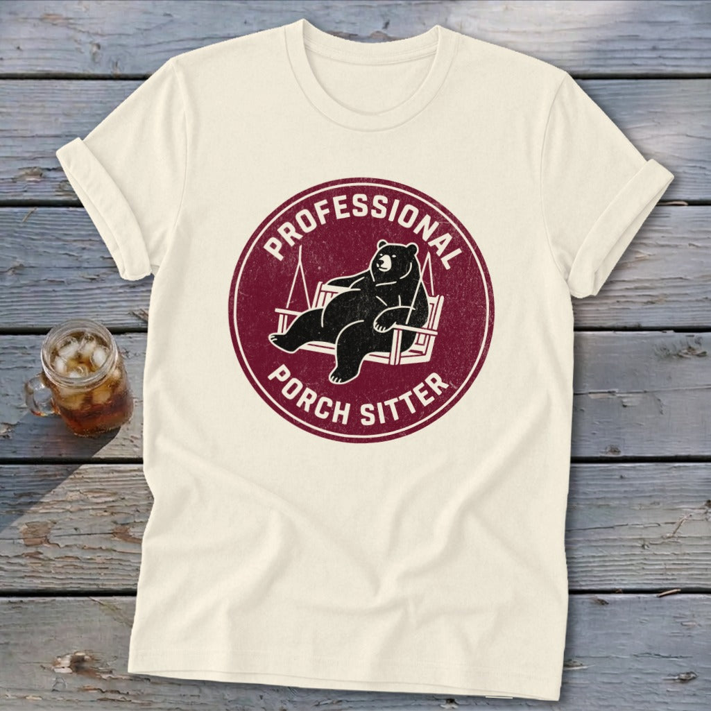 Cream t-shirt with a maroon circular graphic featuring a bear relaxing on a porch swing and the text Professional Porch Sitter.
