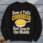 Black crewneck sweatshirt featuring a graphic with yellow text reading Some of Y'all's Cornbread Ain't Done in the Middle and a skillet of cornbread.
