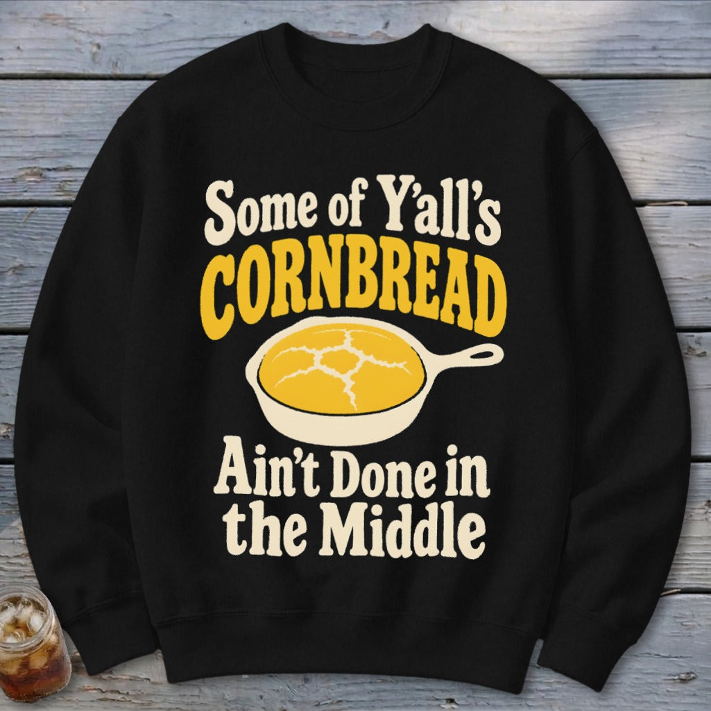 Black crewneck sweatshirt featuring a graphic with yellow text reading Some of Y'all's Cornbread Ain't Done in the Middle and a skillet of cornbread.
