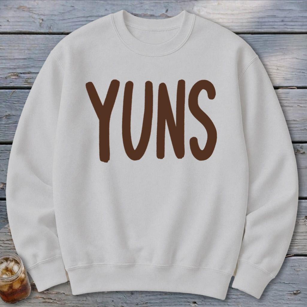 White sweatshirt with brown "YUNS" text and a partial view of a drink.