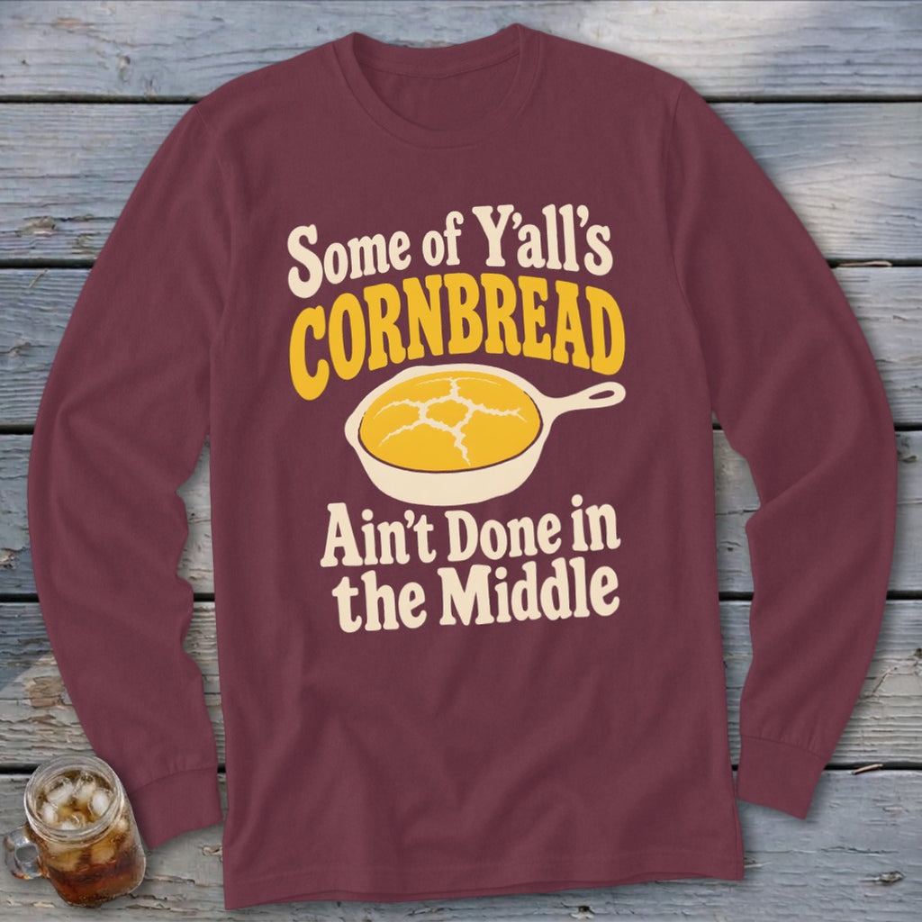 Maroon long-sleeve t-shirt with text stating "Some of Y'all's Cornbread Ain't Done in the Middle" and a graphic of a cornbread skillet.