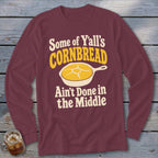 Maroon long-sleeve t-shirt with text stating "Some of Y'all's Cornbread Ain't Done in the Middle" and a graphic of a cornbread skillet.