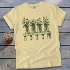 Light yellow t-shirt with a green graphic of four mason jars filled with wildflowers on a shelf.