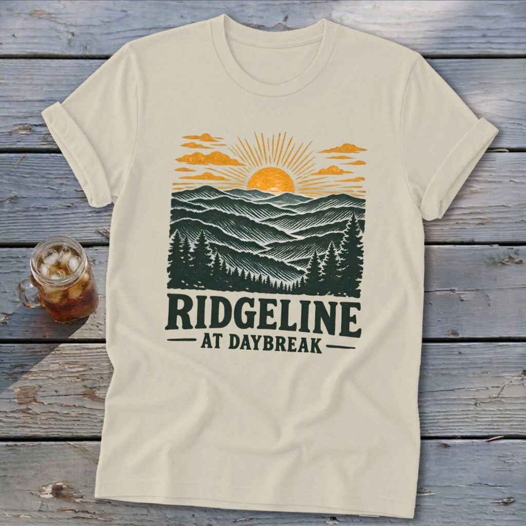 Cream t-shirt with a graphic of mountains at sunrise and the text "RIDGELINE AT DAYBREAK".