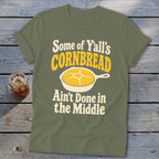 An olive green t-shirt with text that reads Some of Y'all's Cornbread Ain't Done in the Middle and a graphic of a skillet.