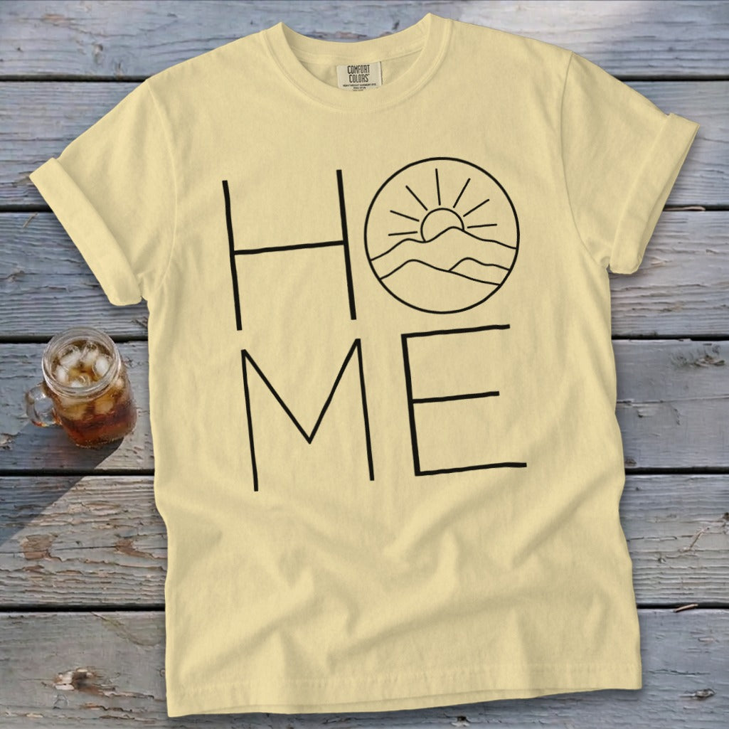 Pale yellow t-shirt with black text reading HOME, where the O is replaced by a mountain sunrise illustration.
