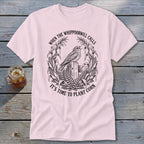 A light pink t-shirt with a vintage-style black illustration of a bird and corn stalks, featuring the text "When the whippoorwill calls it's time to plant corn".