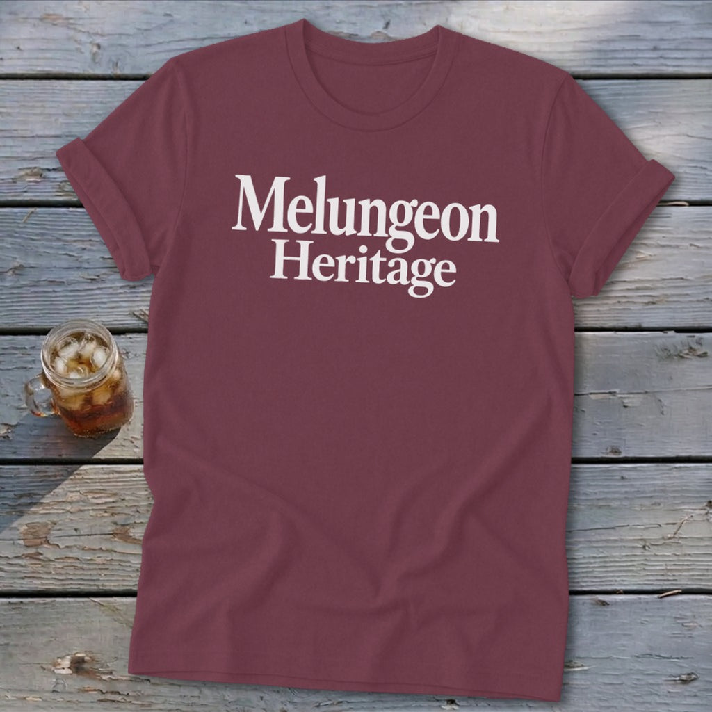 Maroon crewneck t-shirt with rolled sleeves featuring white text reading Melungeon Heritage on a weathered wooden surface.