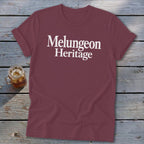 Maroon crewneck t-shirt with rolled sleeves featuring white text reading Melungeon Heritage on a weathered wooden surface.