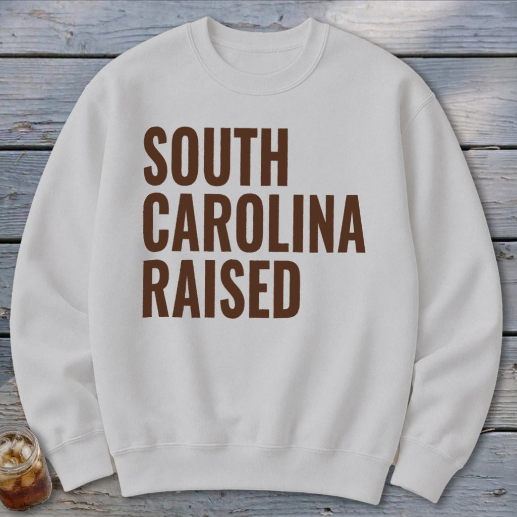 White crewneck sweatshirt with "SOUTH CAROLINA RAISED" text in brown.