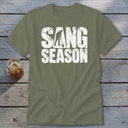 Olive green crewneck t-shirt featuring the distressed white text SANG SEASON, centered on a rustic wooden table.